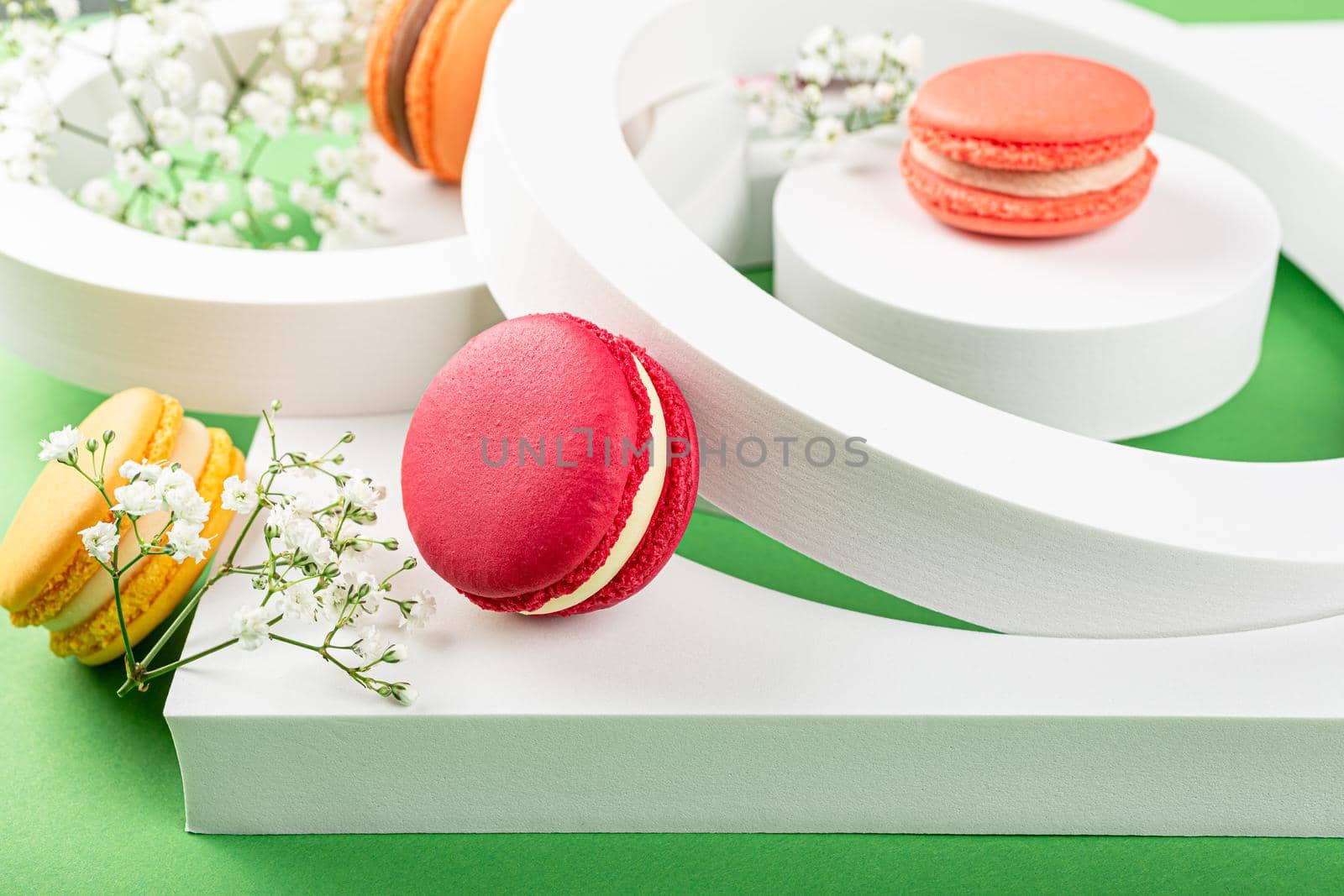 Beautiful festive composition macaron or macaroon cookies with white circles and flowers on green background, colorful almond small cakes, modern greetings card, selective focus