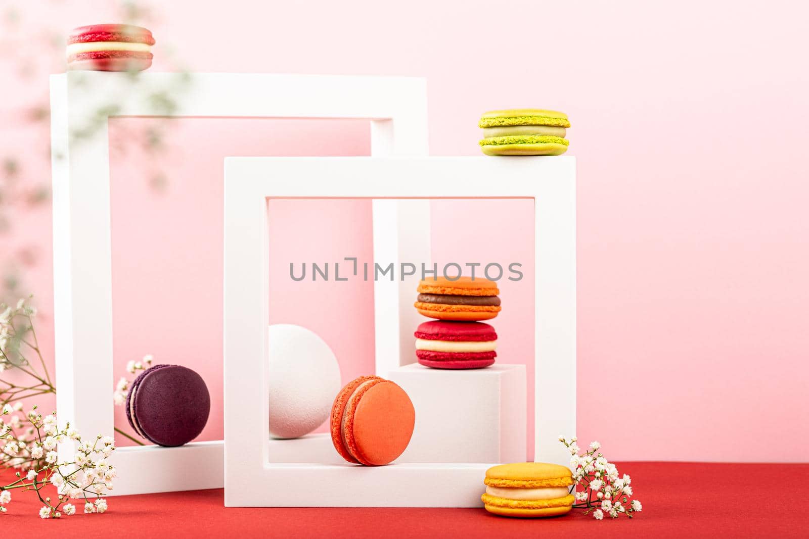 Colorful french macaron dessert. Set of various different tastes and color macaroon cookies with square shapes and flowers on pink background. Festive greeting card concept with copy space