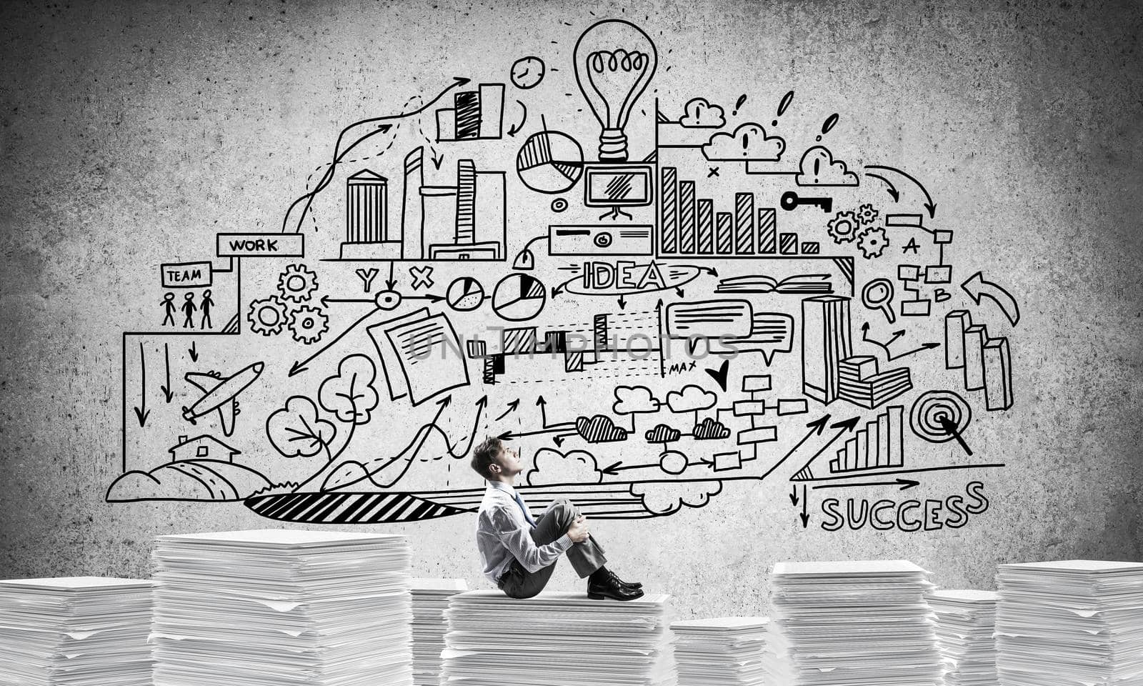 Businessman looking away while sitting on pile of documents against business-plan information on background. Mixed media.