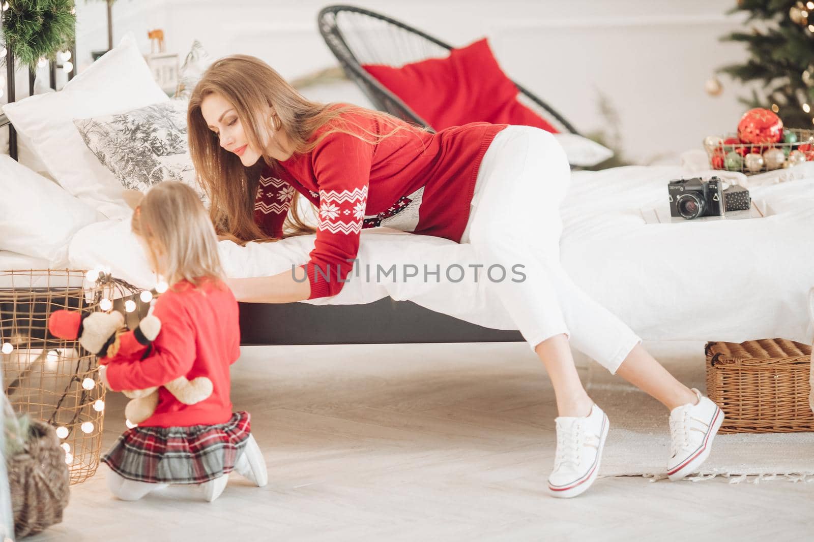 Stock photo of loving mother in green dress giving her little daughter in pyjama dress a Christmas present. They are next to beautifully decorated Christmas tree under snowfall.