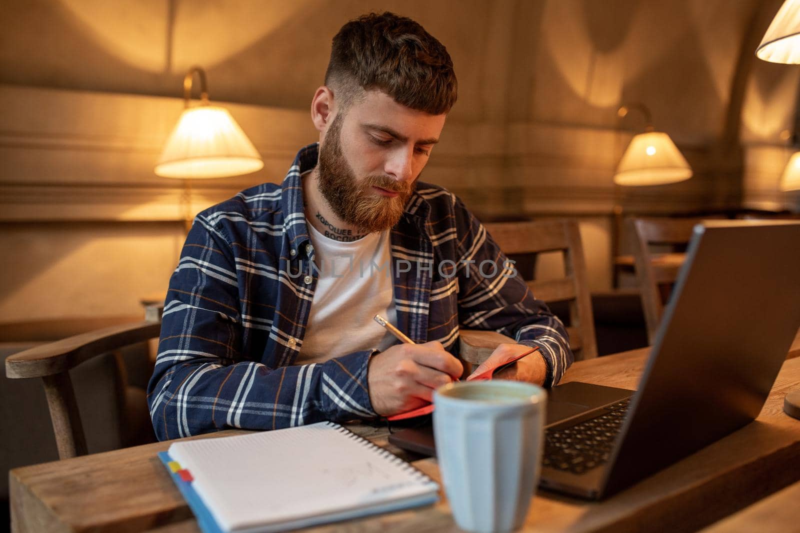 Casual business man or freelancer planning his work on notebook, working on laptop computer with smart phone, cup of coffee on table at coffee shop or home office, working from cafe concept
