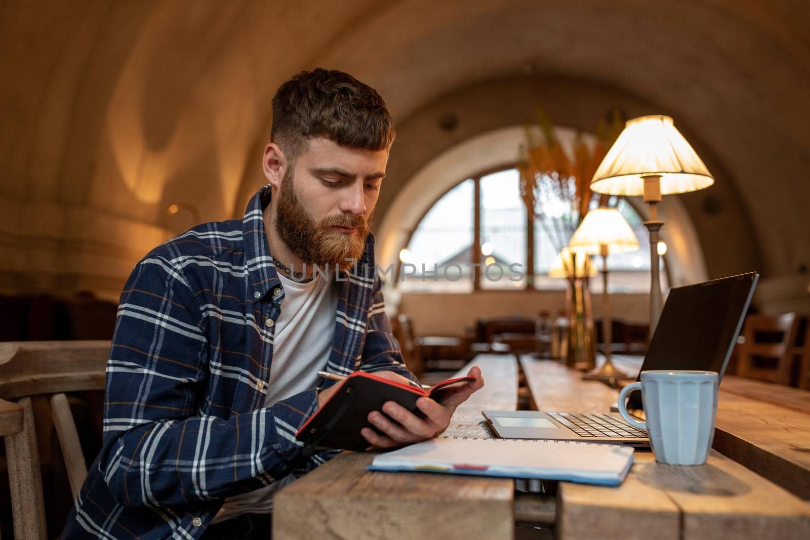 Casual business man or freelancer planning his work on notebook, working on laptop computer with smart phone, cup of coffee on table at coffee shop or home office, working from cafe concept