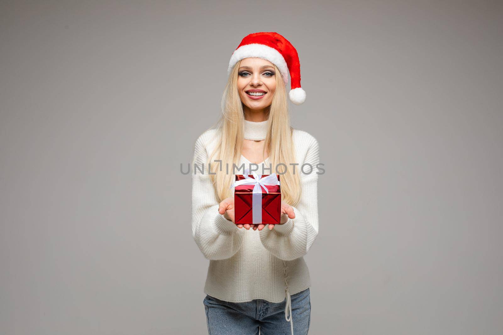 pretty caucasian woman holds a small red box with a present and poses for the camera isolated on white background by StudioLucky