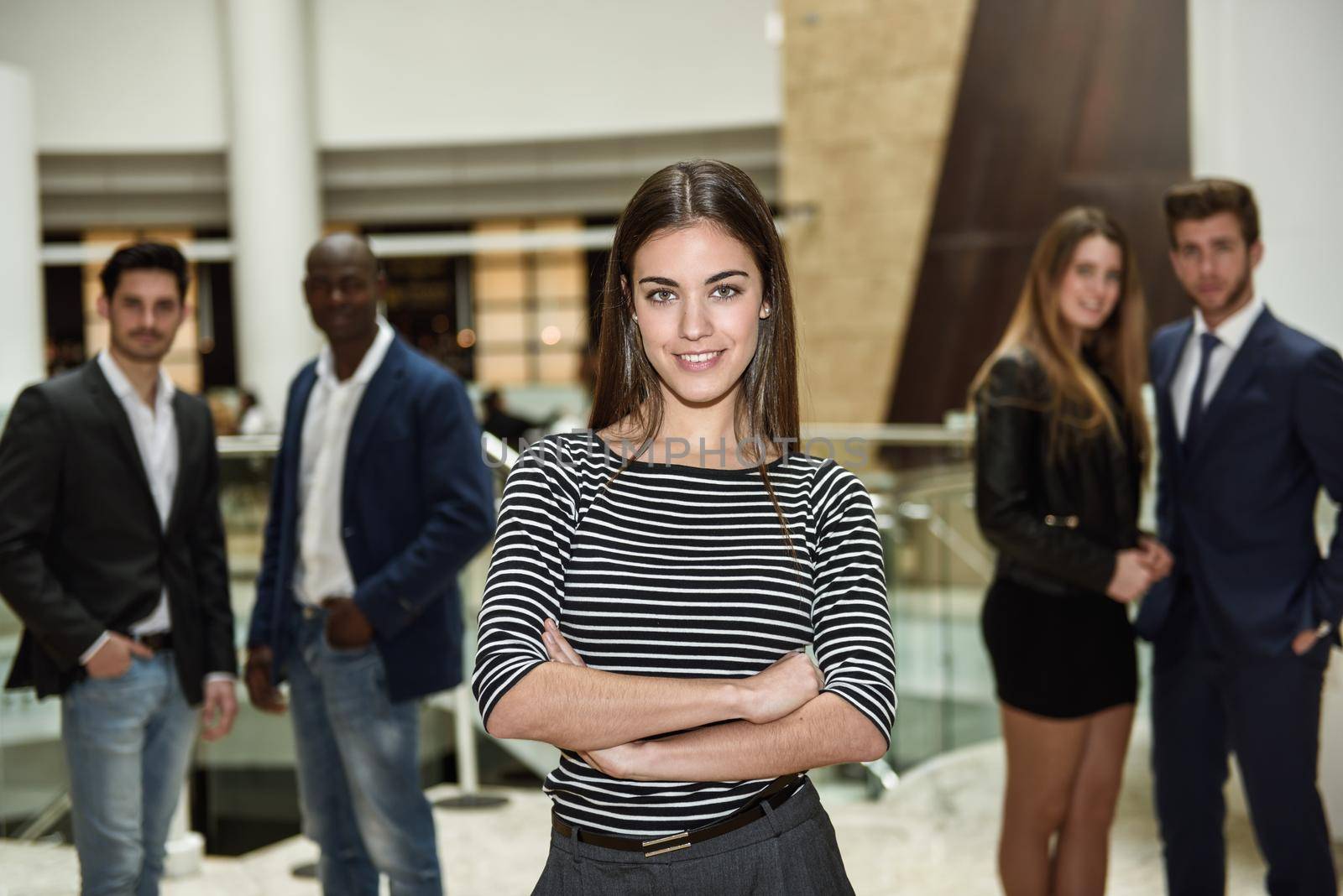 Young businesswoman leader looking at camera in office building. Group of multi-ethnic people in the background