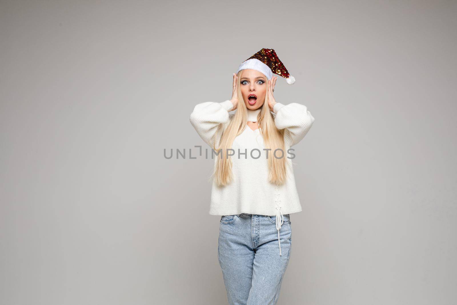 Close-up studio photo of a beautiful young lady in Santa hat cupping hands around mouth and making faces