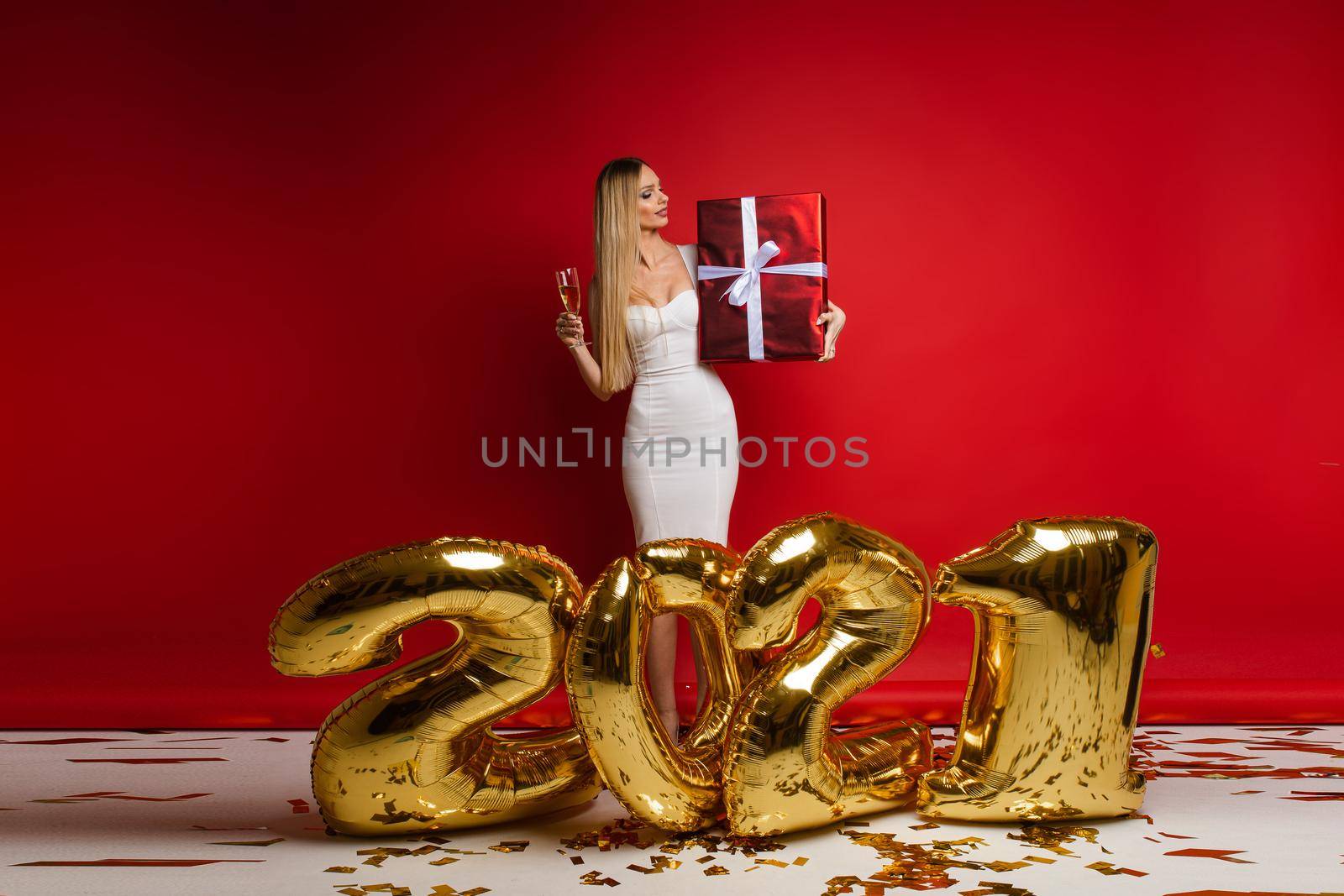 cheerful caucasian young woman in white dress holds a big red box with a gift, picture isolated on red background