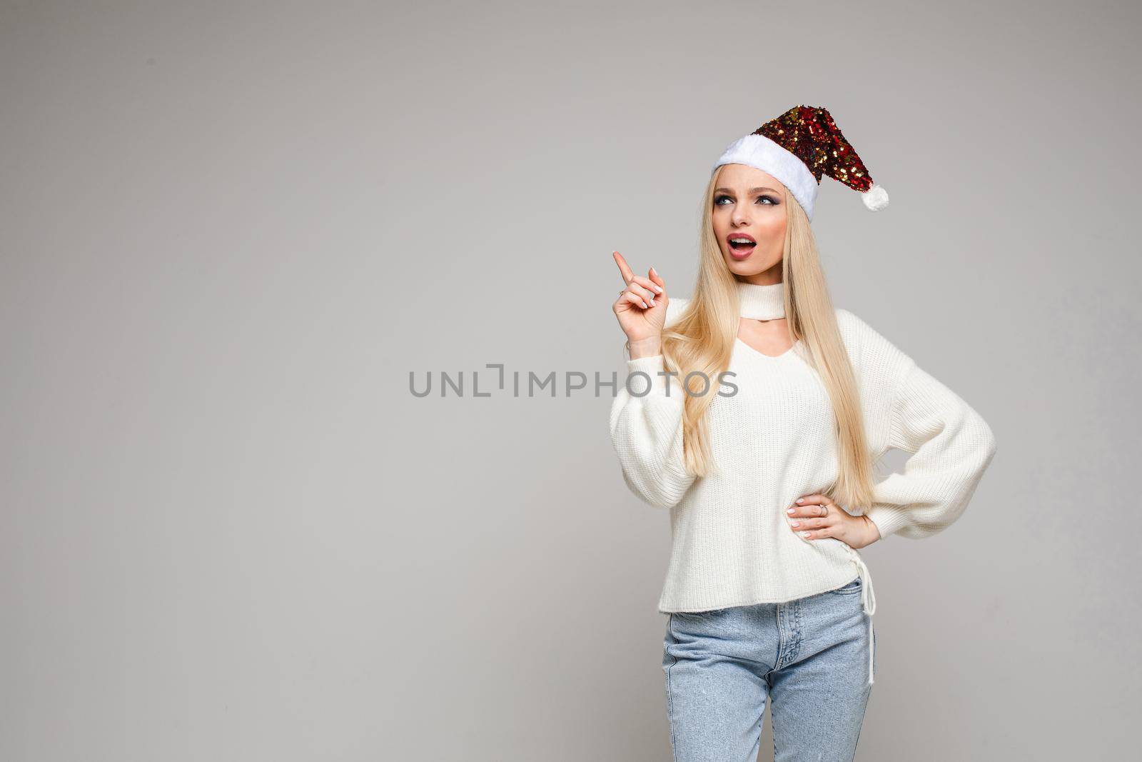 Portrait of beautiful young woman in Santa hat posing in studio, isolated on grey background. Holiday concept