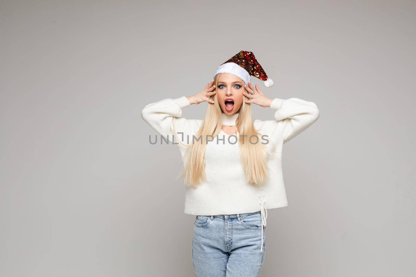 scared caucasian female with long fair hair in white sweater, blue jeans and red christmas hat