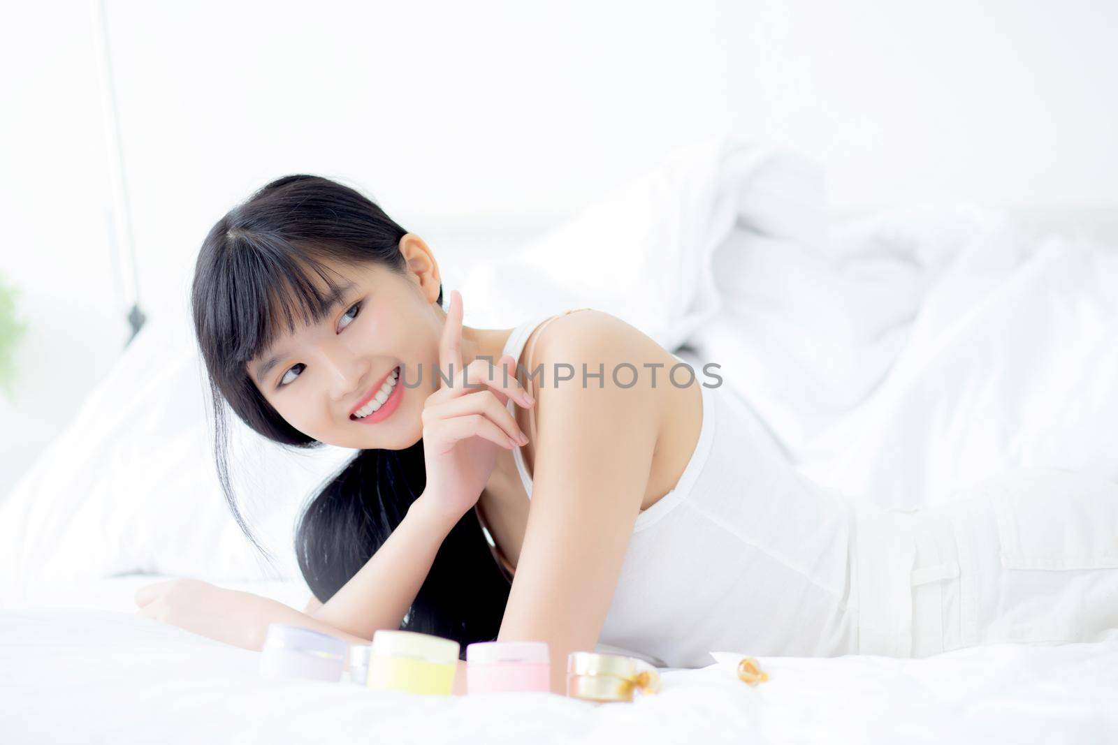 Beautiful of young asian woman smiling and lying on bed at bedroom, beauty of girl touch cheek with hygiene and healthy, cream and lotion, cosmetic and makeup, skin care and lifestyles concepts.