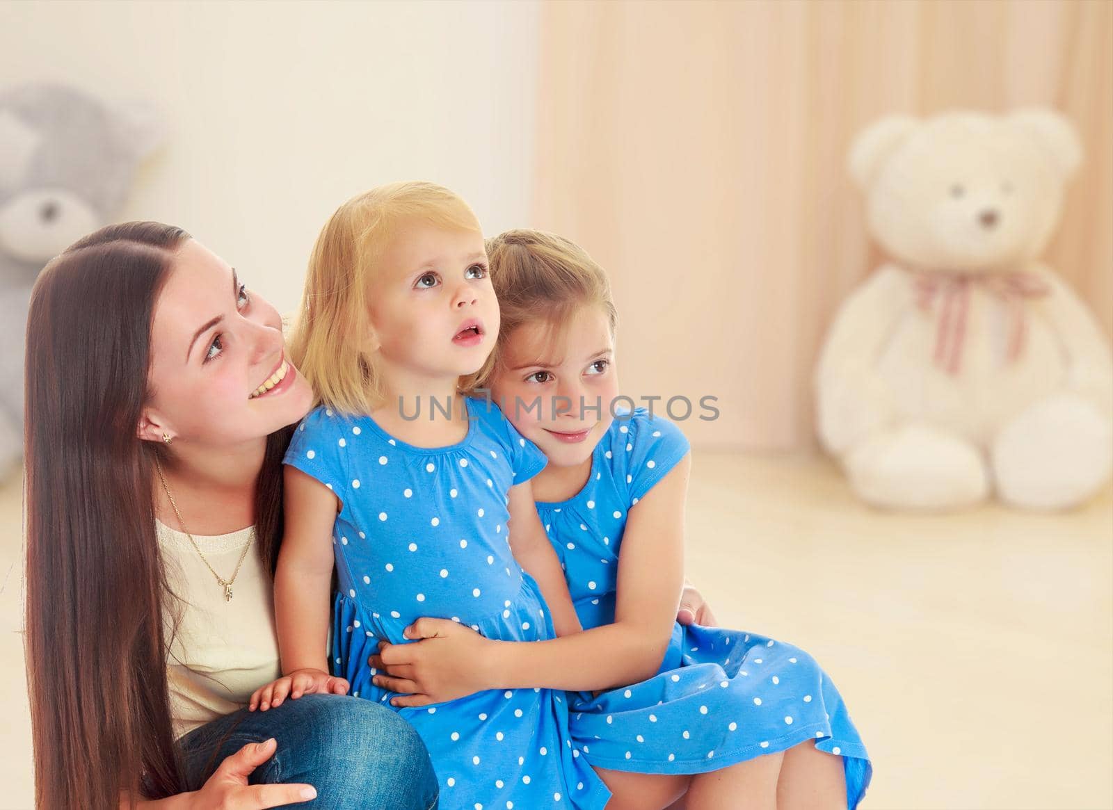 Beautiful young mother with her two daughters. All look up.In the background children's room where the sitting Teddy bear.