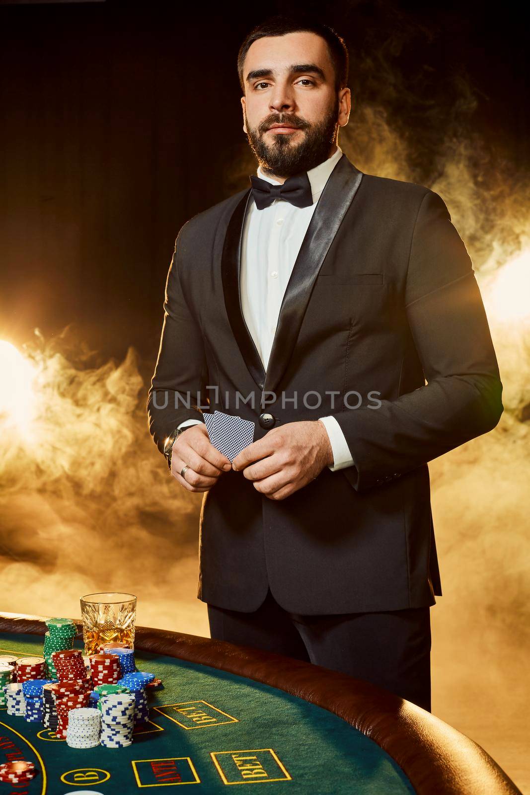A young man in a business suit standing near poker table. Man gambles. The player at the gaming table playing cards.