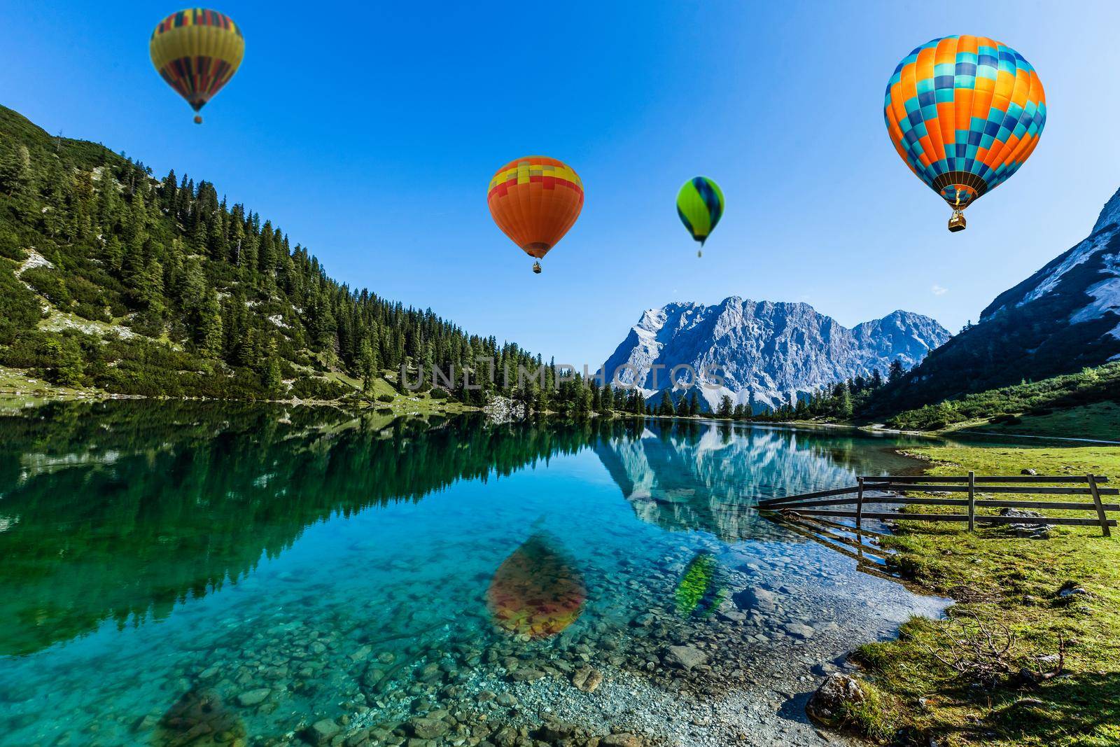Colorful hot air balloons flying over the lake surrounded by mountains. large multi-colored balloons slowly rising against blue sky. Travel, adventure, festival