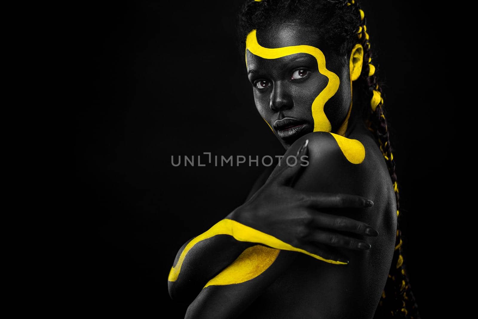 Face art. Woman with black and yellow body paint. Young african girl with colorful bodypaint. An amazing afro american model with yellow makeup.