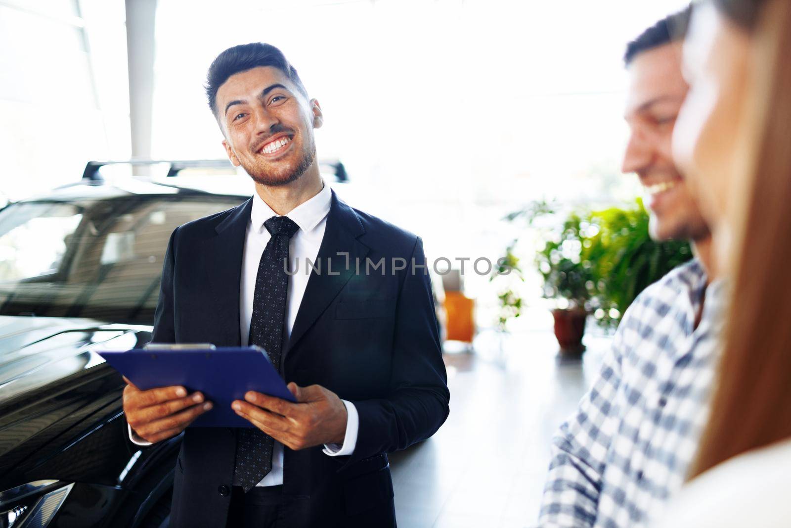 Man car salesman telling about the features of the new car to the couple at dealership