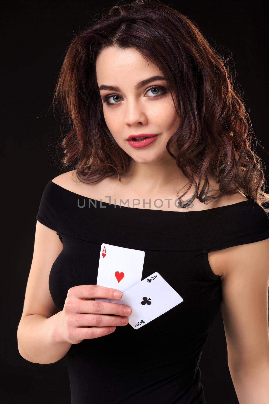 Young woman playing in the gambling on black background. Sexy brunette in a dress with two aces in her hand