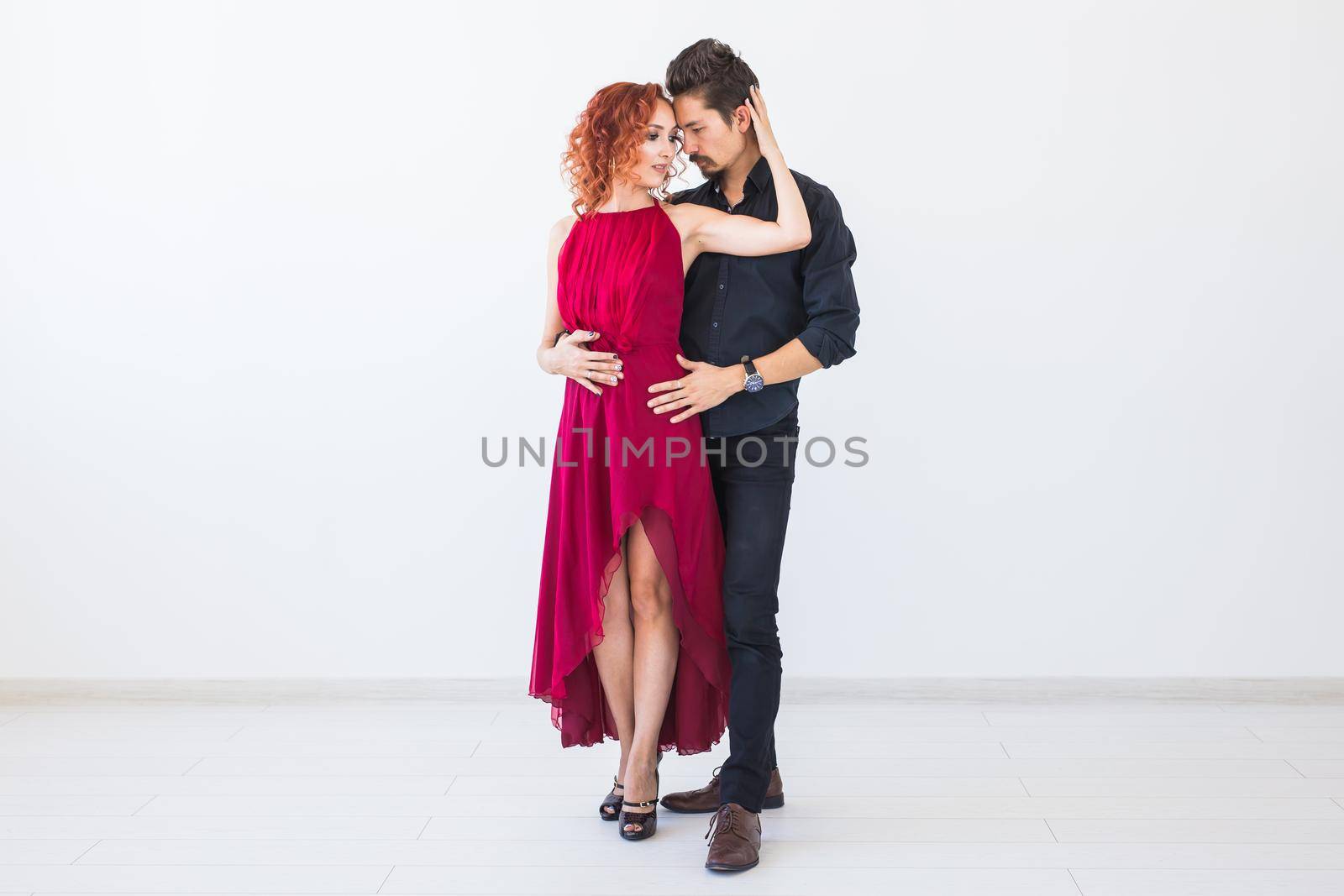 Social dance, bachata, kizomba, salsa, tango concept - Woman dressed in red dress and man in a black costume over white background.