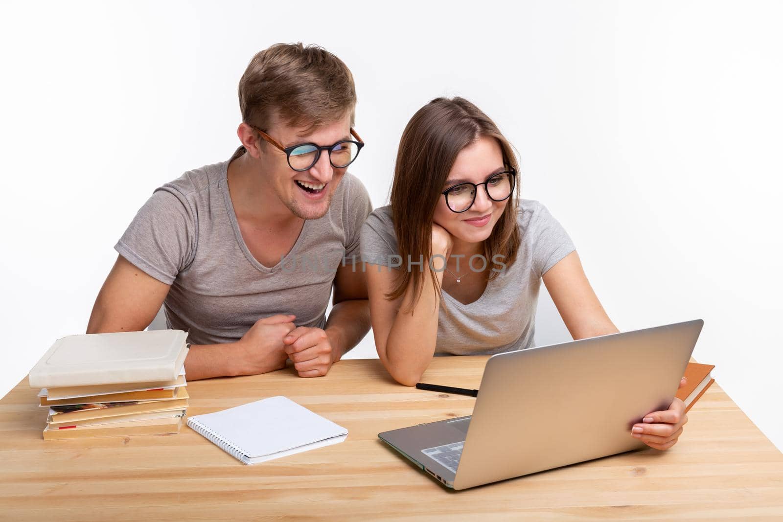 People and education concept - Two happy funny students sitting at the wooden table with laptop and books.