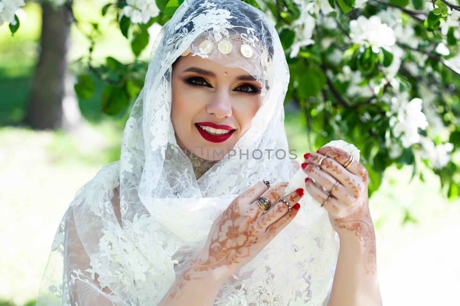 young pretty indian girl in jewelry and veil posing cheerful happy smiling in green park, lifestyle people concept close up