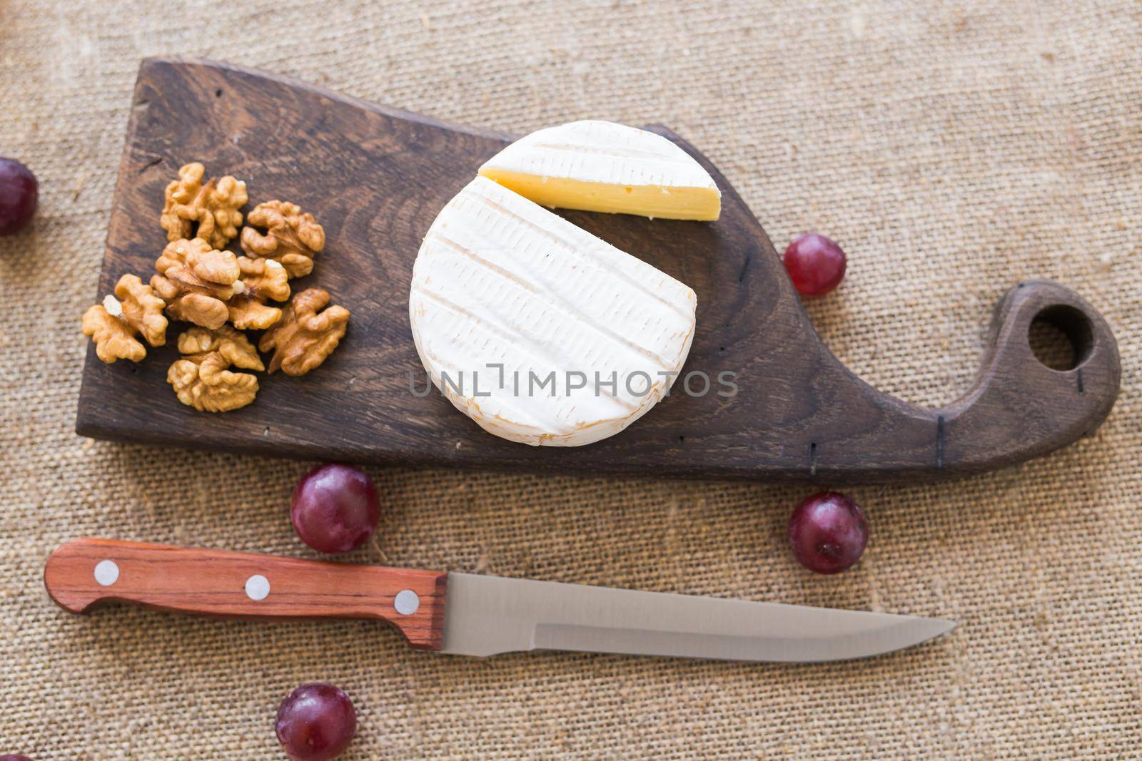 Brie or camembert cheese with nuts and grapes on a wooden board.