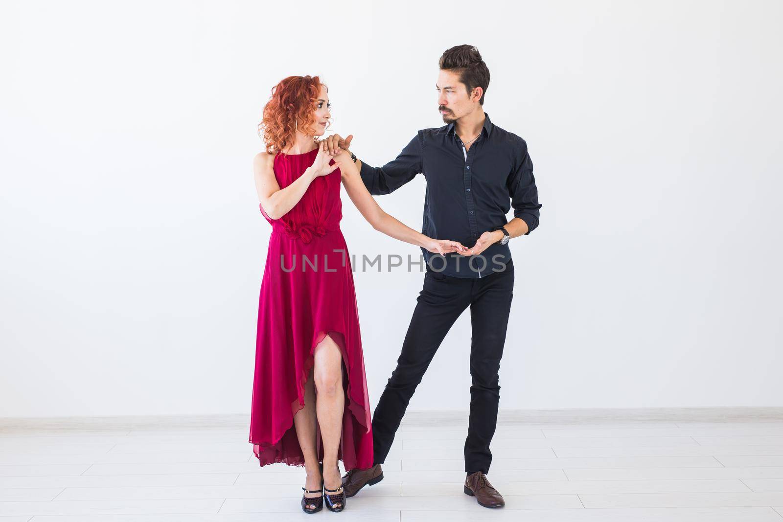 Social dance, bachata, kizomba, salsa, tango concept - Woman dressed in red dress and man in a black costume over white background.