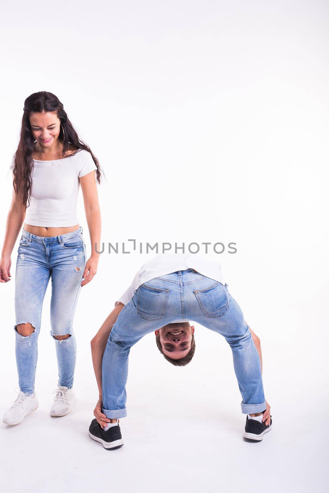 Concept of infantilism, fun and spontaneity - Young crazy mad man fool pose on white background. And pretty girl looks at him and laughs. by Satura86