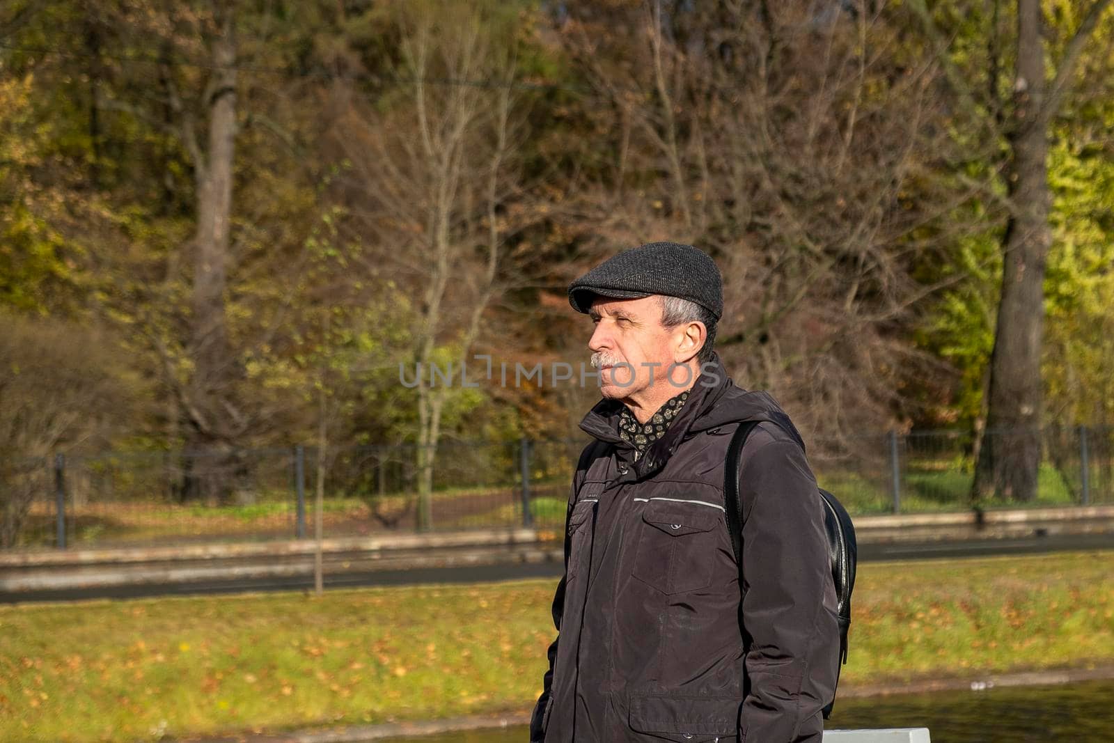 Elderly pensioner stands on beautiful autumn day in city park by OlgaGubskaya