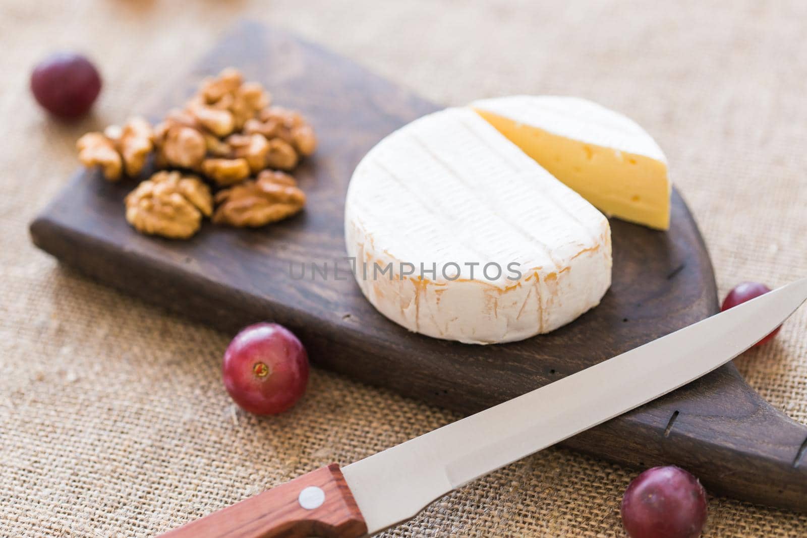 Brie type of cheese. Camembert cheese. Fresh Brie cheese on a wooden board with nuts and grapes. Italian, French cheese. by Satura86