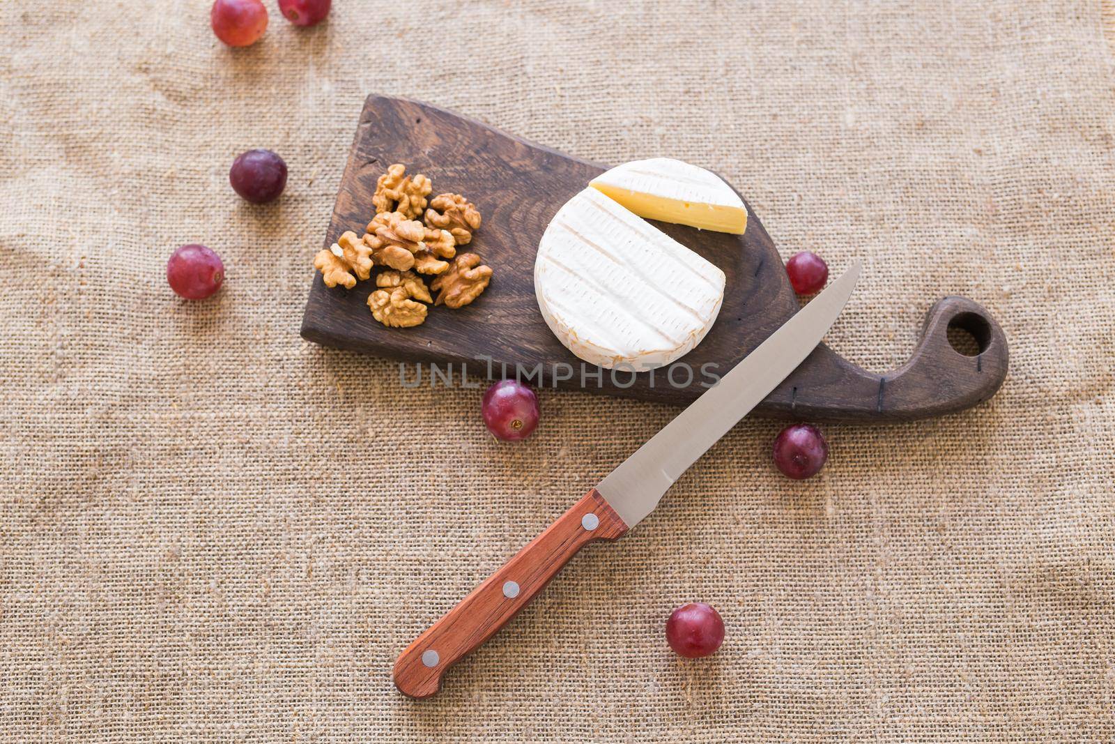 Brie or camembert cheese with nuts and grapes on a board top view. by Satura86