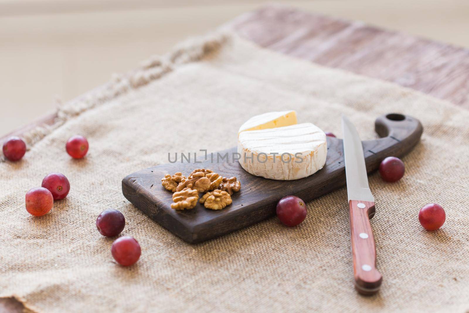 Brie or camembert cheese with nuts and grapes on a wooden board.