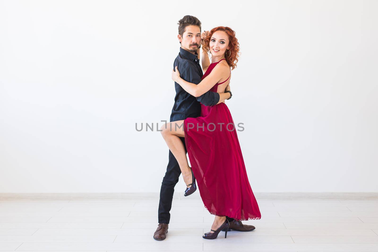 Social dance, bachata, kizomba, salsa, tango concept - Woman dressed in red dress and man in a black costume over white background.