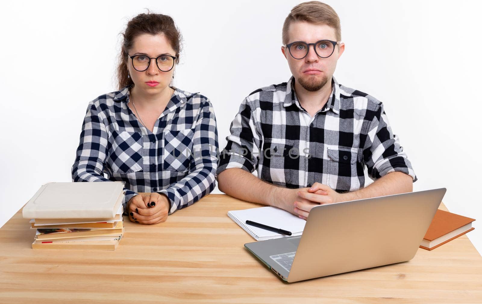 People and education concept - Two sad students dressed in plaid shirt sitting at a table by Satura86