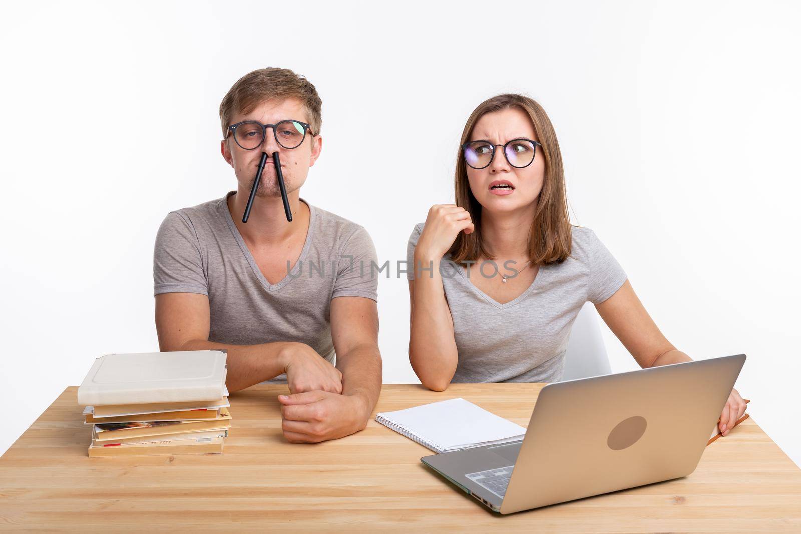 Education, fun and people concept - a couple of young people in glasses look like they are bored of learning homework and make a stupid jokes by Satura86