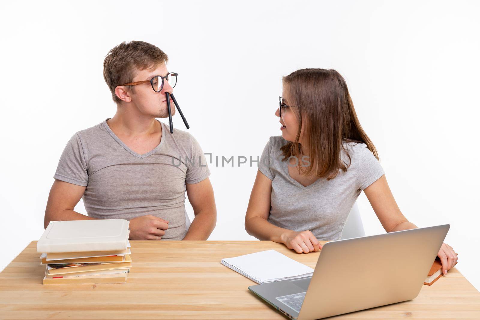 Education, fun and people concept - a couple of young people in glasses look like they are bored of learning homework and guy is making a stupid jokes, girl is laughing at him