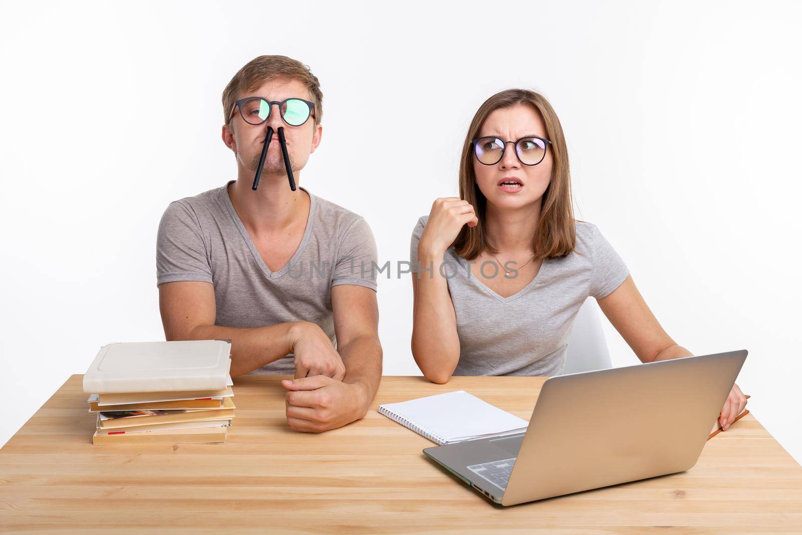 Education and people concept - a couple of young people in glasses look like they are bored of learning homework and make a stupid jokes.