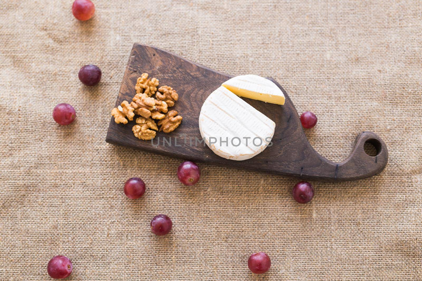 Brie or camembert cheese with nuts and grapes on a wooden board top view. by Satura86