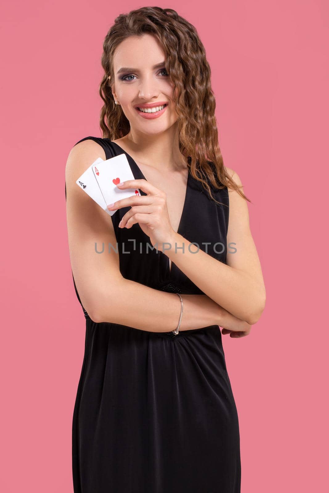 Young woman in black dress holding two aces in hand against on pink background. Studio shot