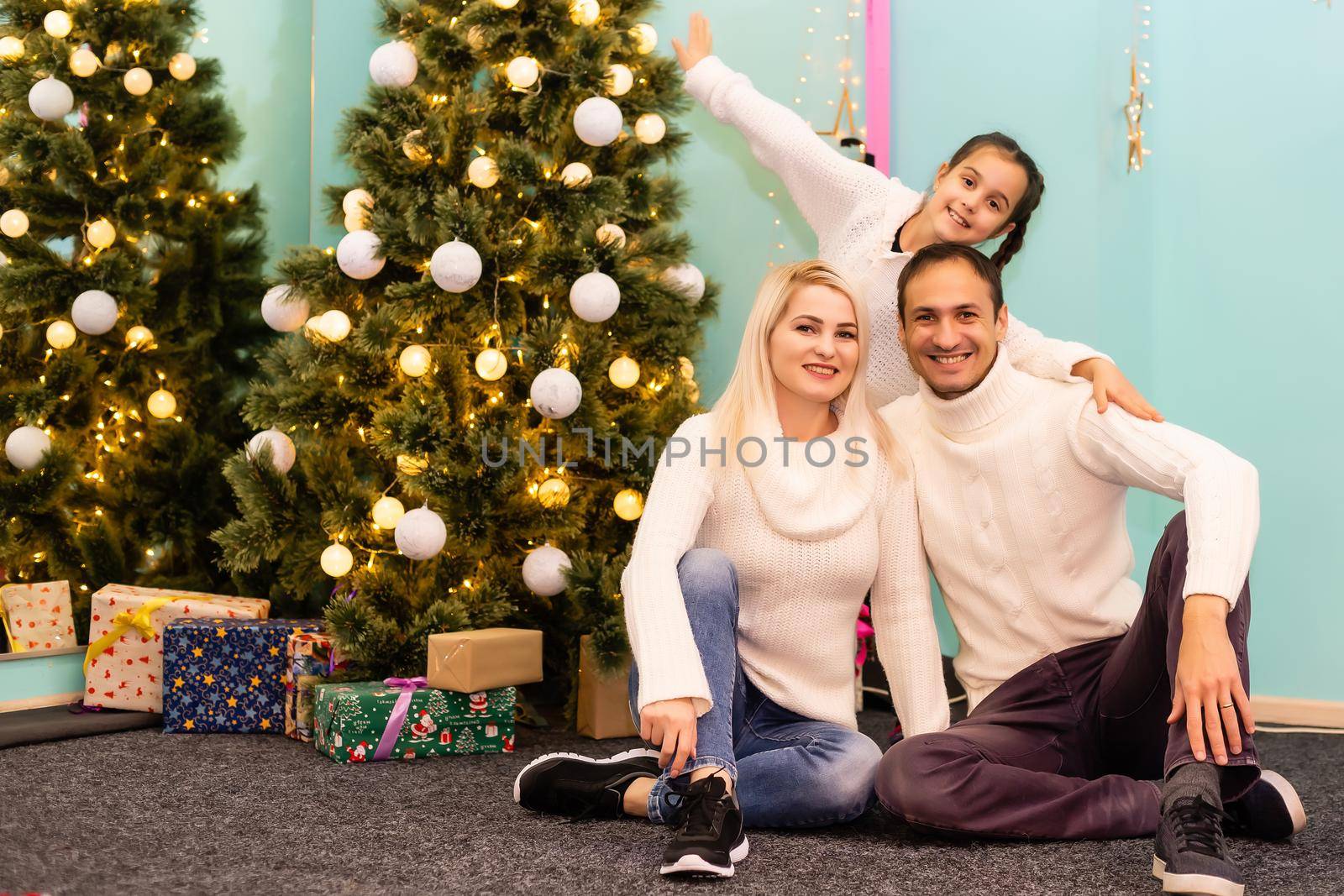 Christmas. Family. Happiness. dad, mom and daughter in Santa hats looking at camera and smiling on the floor at home by Andelov13