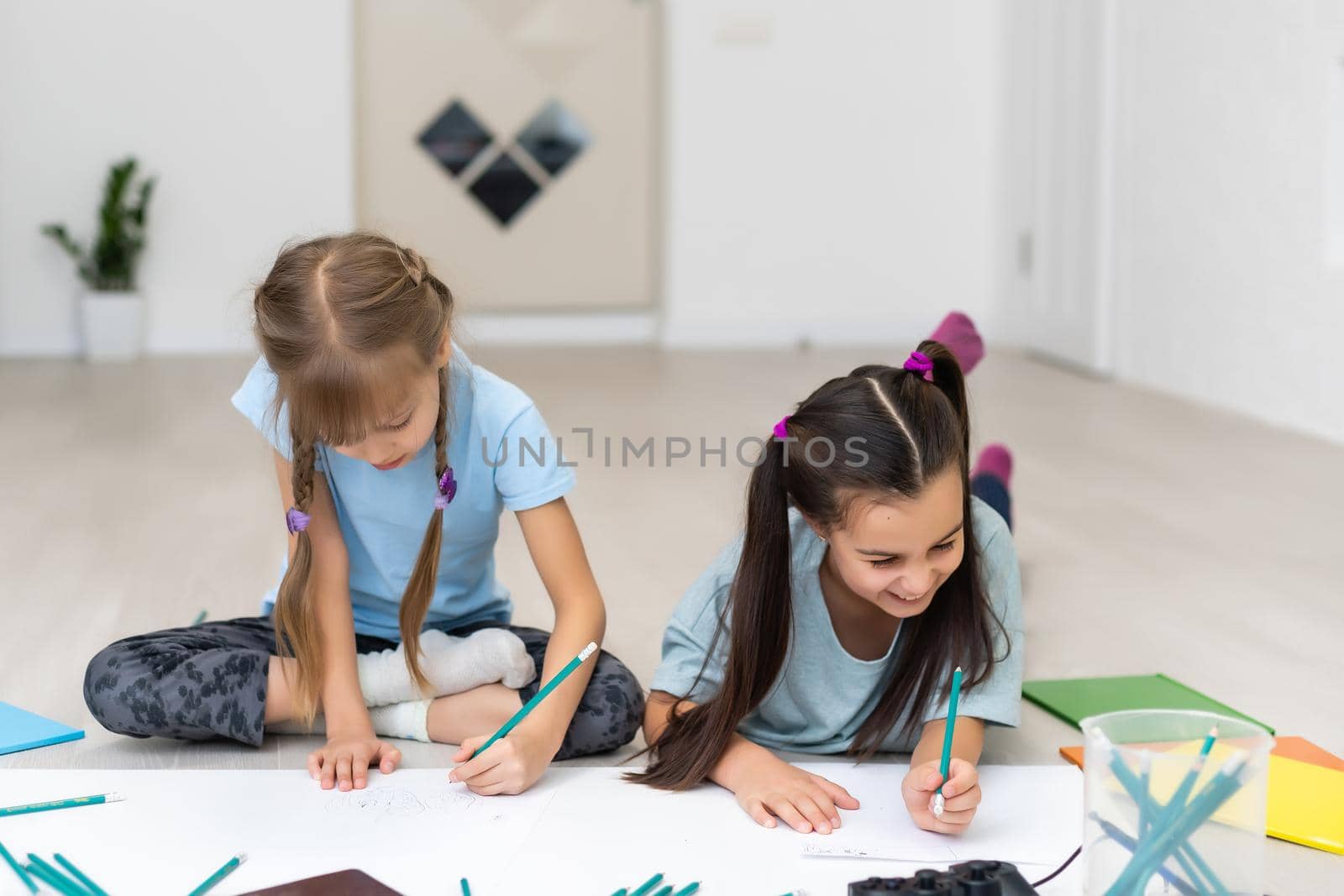 Cute children are painting and smiling while lying on the floor at home