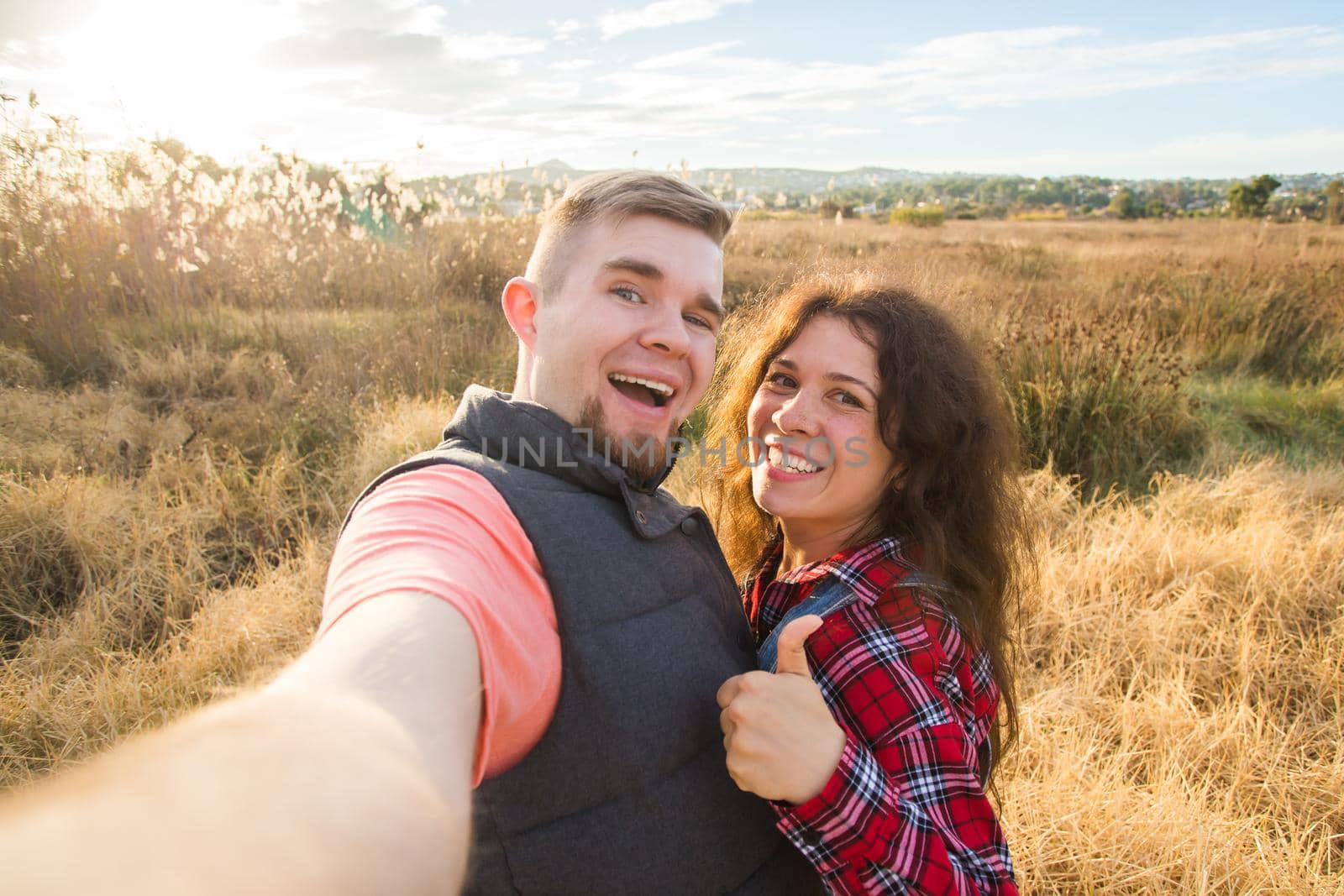 Travel, tourism and nature concept - Smiling couple taking selfie on field and showing thumbs up.