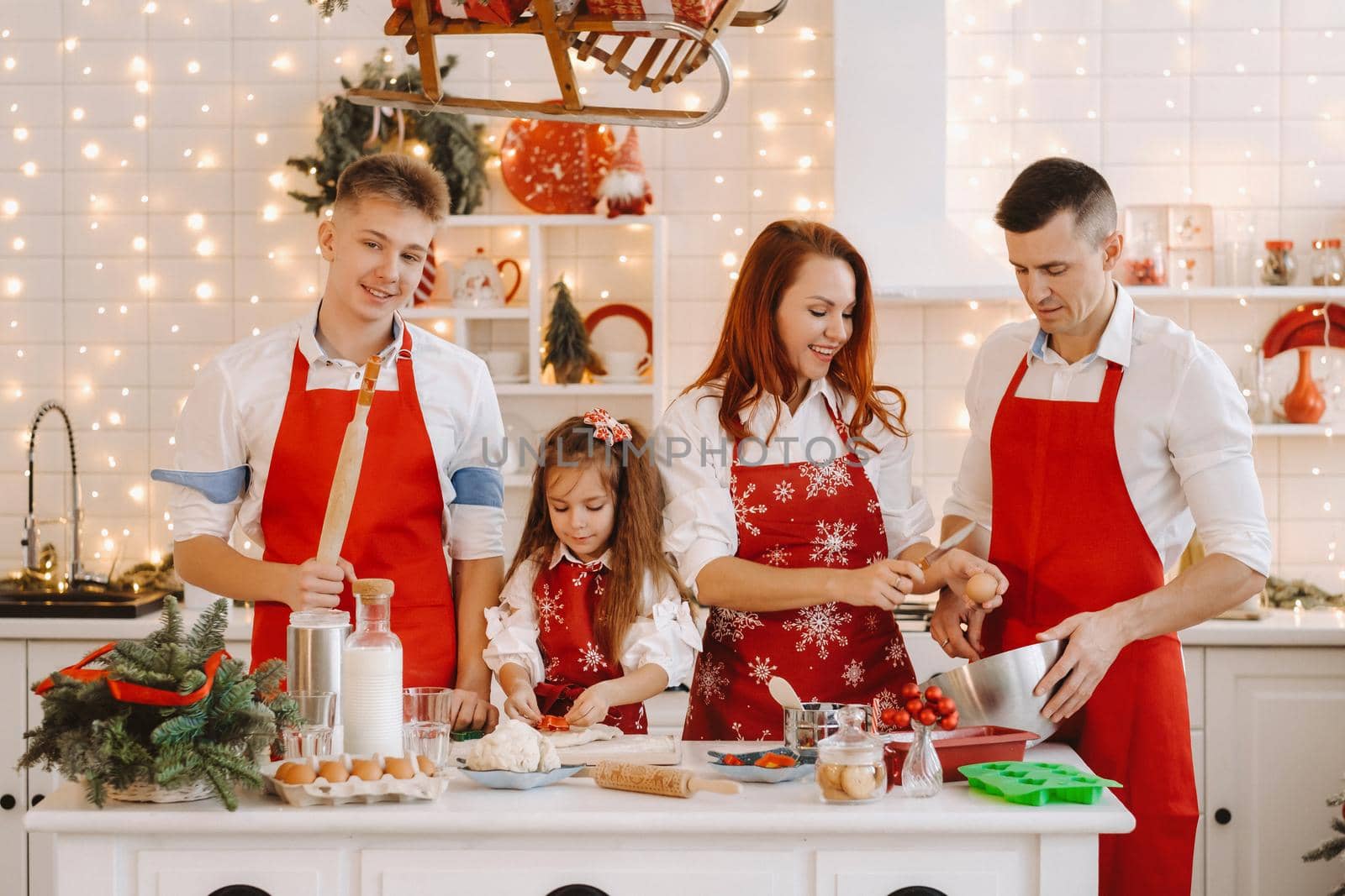 A happy family is standing in the Christmas kitchen and preparing dough for making cookies.