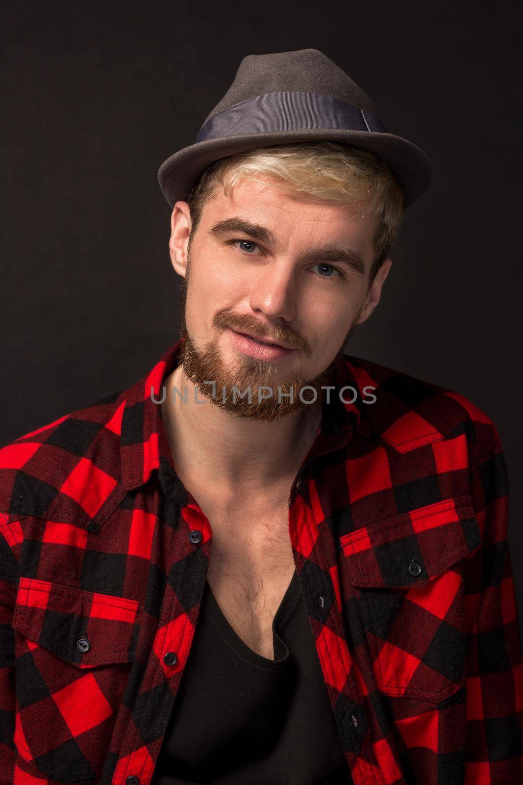 Man in red shirt in cage with hat on black background. Studio shot