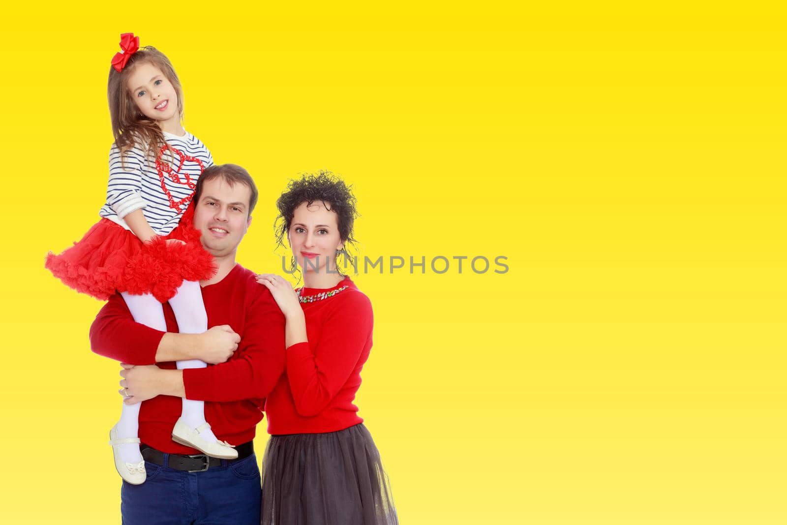 Happy young family dad mom and a little girl in bright red outfits . Dad holds daughter on hands.
