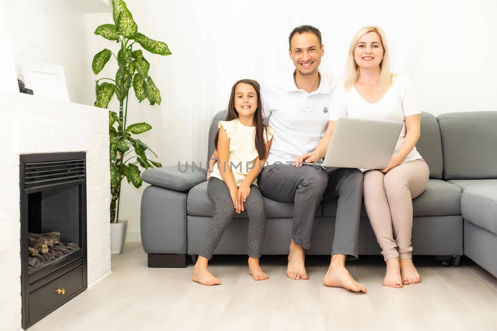 Happy family with kid girl having fun using laptop together sitting on sofa, parents and child daughter laughing relaxing at home with computer watching funny internet video, making online call by Andelov13
