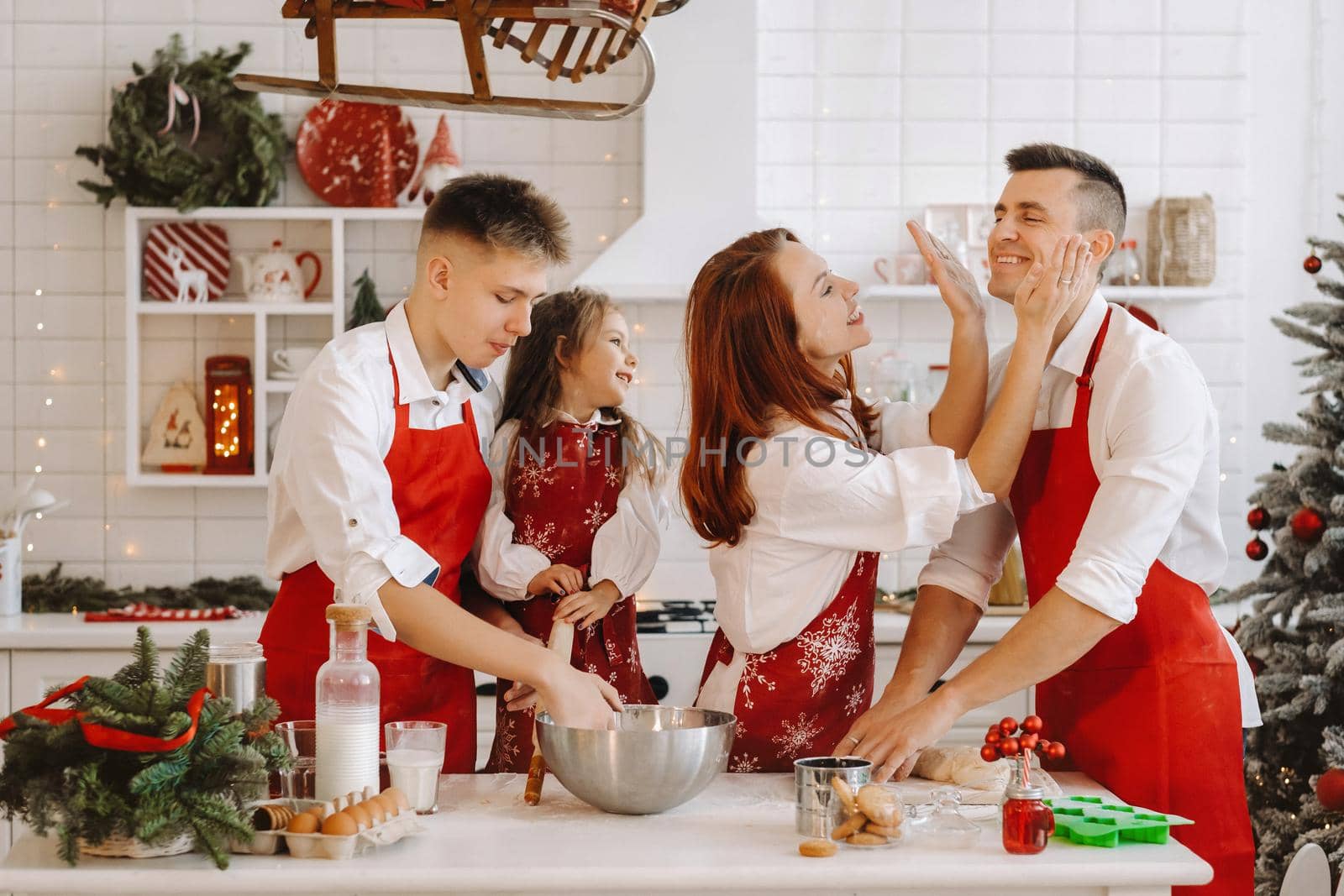 A happy family is standing in the Christmas kitchen and smearing each other with flour.