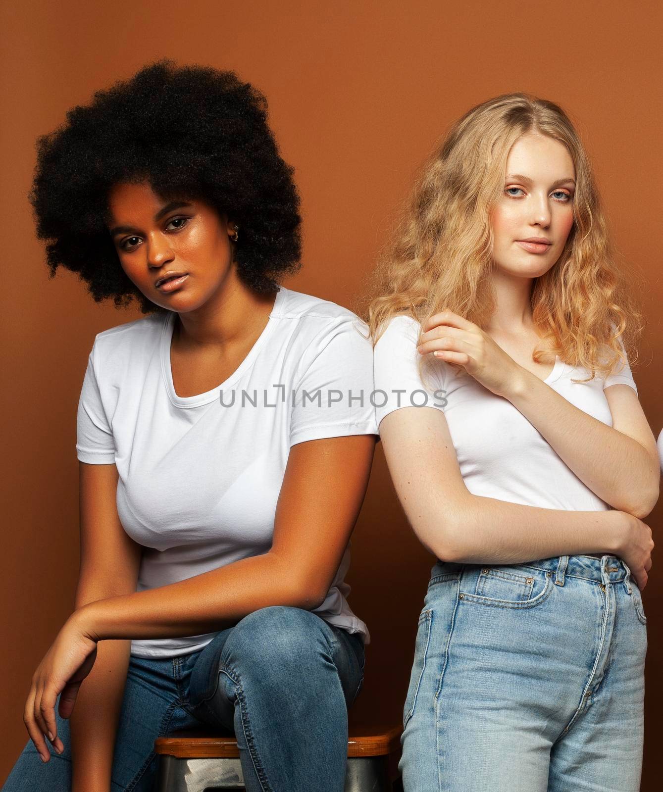 young pretty african and caucasian women posing cheerful together on brown background, lifestyle diverse nationality people concept by JordanJ