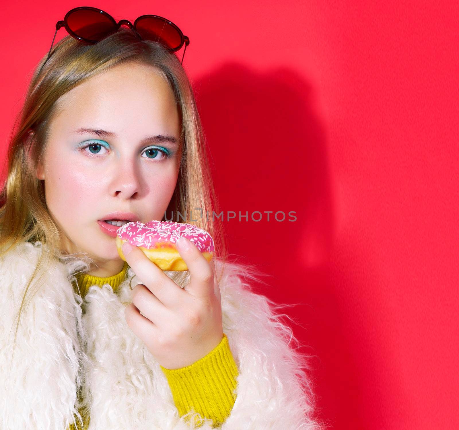 little cute blond teenage girl posing in fashion style with donut on red background, lifestyle people concept close up