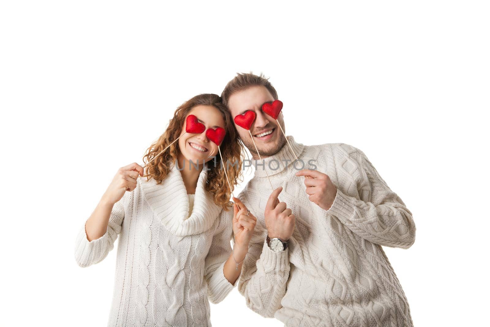 Portrait of joyful couple holding red hearts by their eyes and laughing