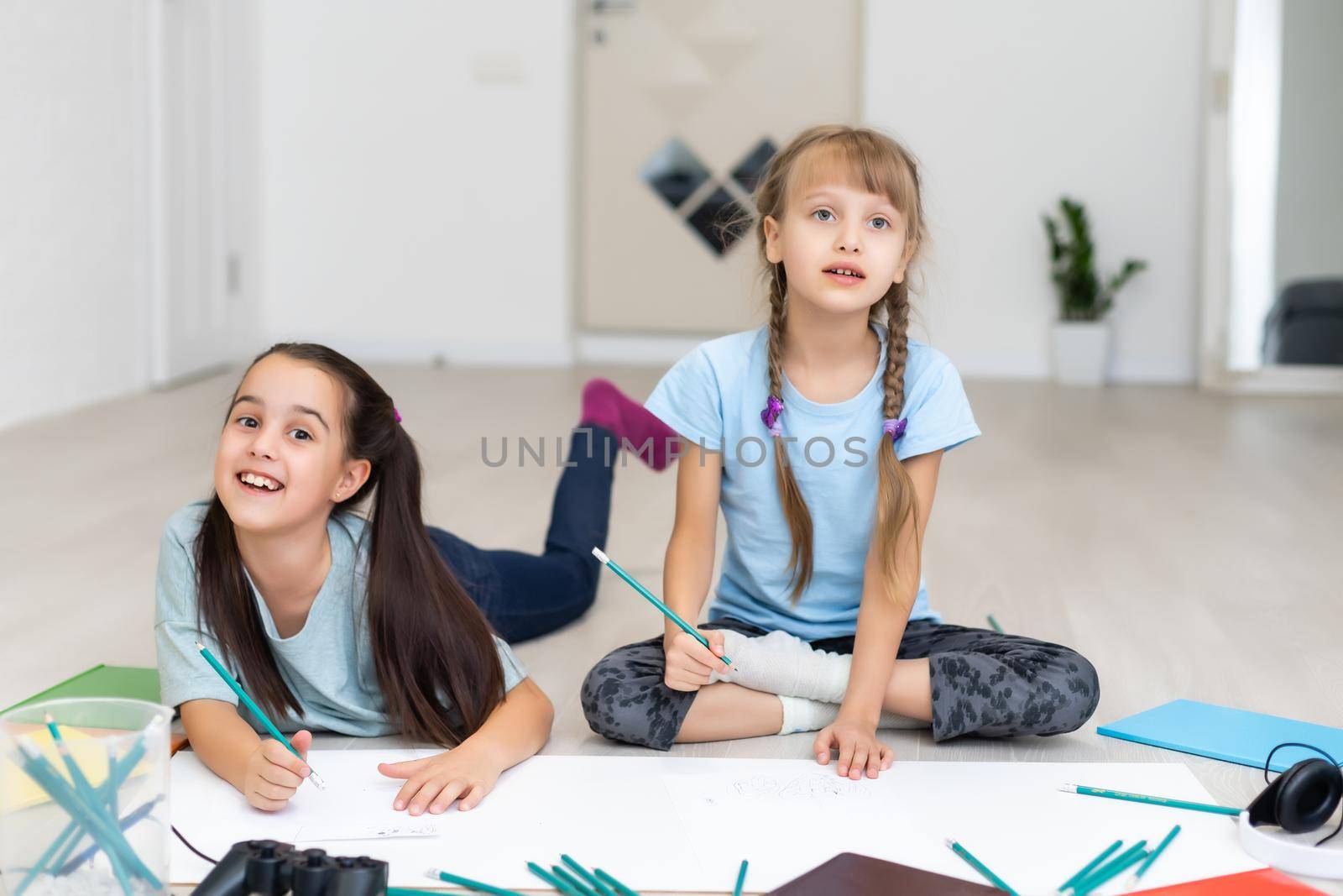 two little girls sisters lie on the floor of the house and draw with colored pencils on paper. children do creative homework after school. by Andelov13