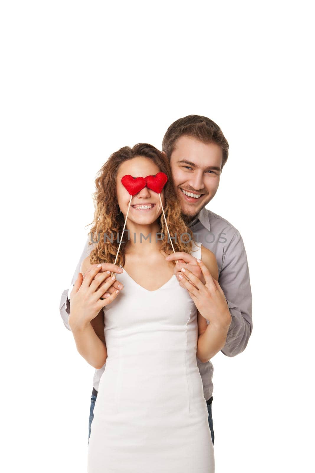 Portrait of joyful couple holding red hearts by their eyes and laughing