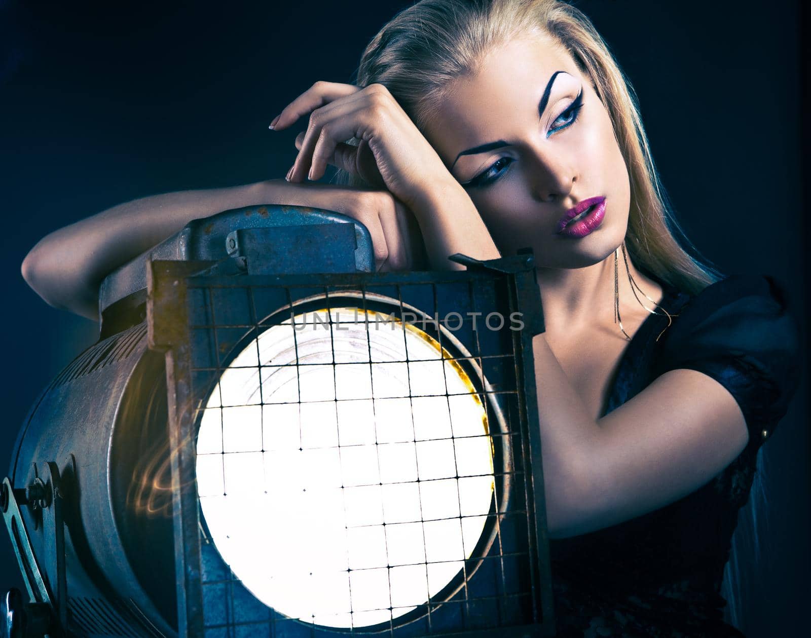 Sexy young woman with old floodlight over dark background